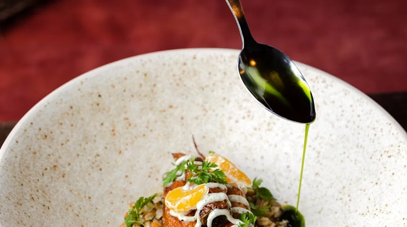 A plated dish being finished with a drizzle of oil